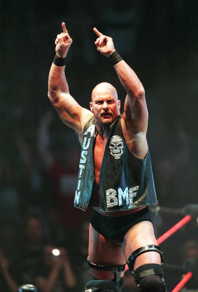 Steve Austin, stands on the middle turnbuckle, arms raised and hands holding up middle fingers only, as he scowls at the crowd.